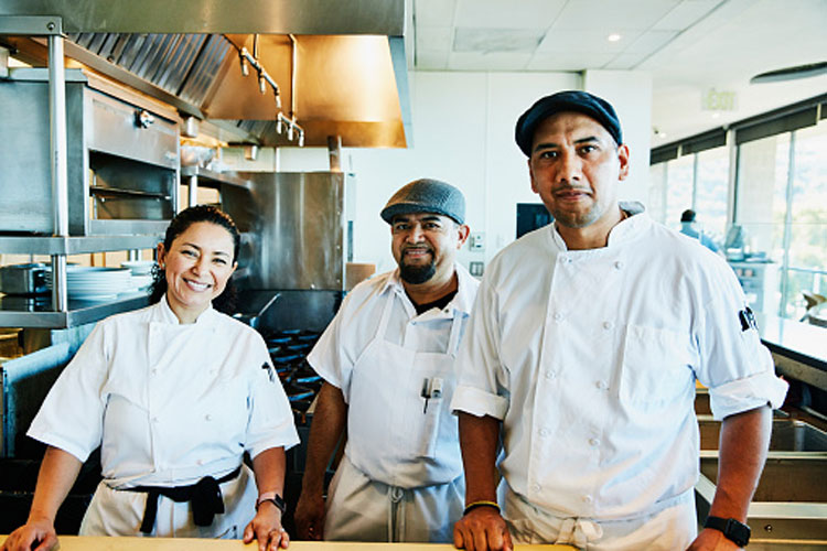 Portrait of female chef with kitchen staff in restaurant kitchen